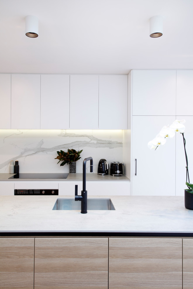 Design ideas for a small modern galley open plan kitchen in Sydney with an undermount sink, flat-panel cabinets, solid surface benchtops, white splashback, porcelain splashback, black appliances, medium hardwood floors, with island and beige benchtop.