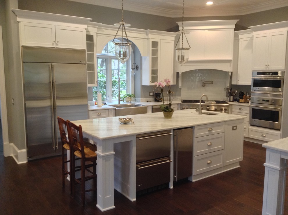 Inspiration for a mid-sized transitional l-shaped medium tone wood floor open concept kitchen remodel in Jacksonville with a farmhouse sink, shaker cabinets, white cabinets, quartzite countertops, white backsplash, subway tile backsplash, stainless steel appliances and an island