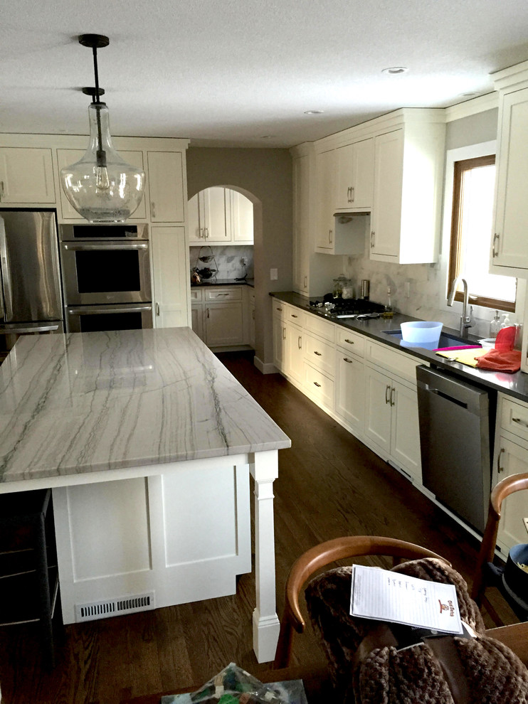 Inspiration for a large transitional dark wood floor and brown floor kitchen remodel in Minneapolis with an undermount sink, shaker cabinets, white cabinets, quartzite countertops, gray backsplash, stone tile backsplash, stainless steel appliances and an island