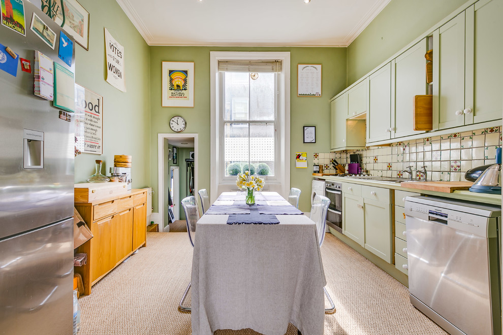 Inspiration for a mid-sized traditional single-wall eat-in kitchen in London with a double-bowl sink, recessed-panel cabinets, green cabinets, wood benchtops, beige splashback, ceramic splashback, stainless steel appliances, carpet, no island, beige floor and green benchtop.