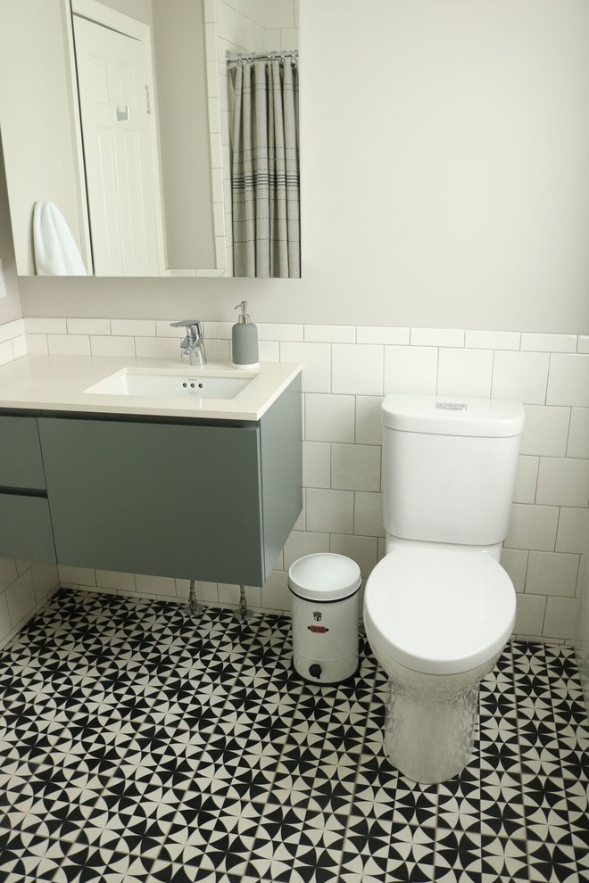 Photo of a mid-sized transitional 3/4 bathroom in Omaha with flat-panel cabinets, grey cabinets, an alcove tub, a shower/bathtub combo, a two-piece toilet, white tile, porcelain tile, grey walls, cement tiles, an undermount sink, engineered quartz benchtops, multi-coloured floor and a shower curtain.
