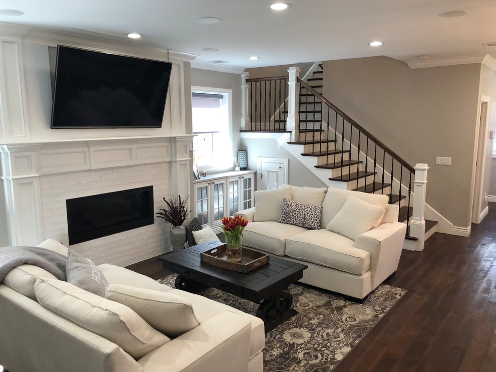 Photo of a large traditional formal open concept living room in Denver with grey walls, medium hardwood floors, a ribbon fireplace, a brick fireplace surround, a wall-mounted tv and brown floor.