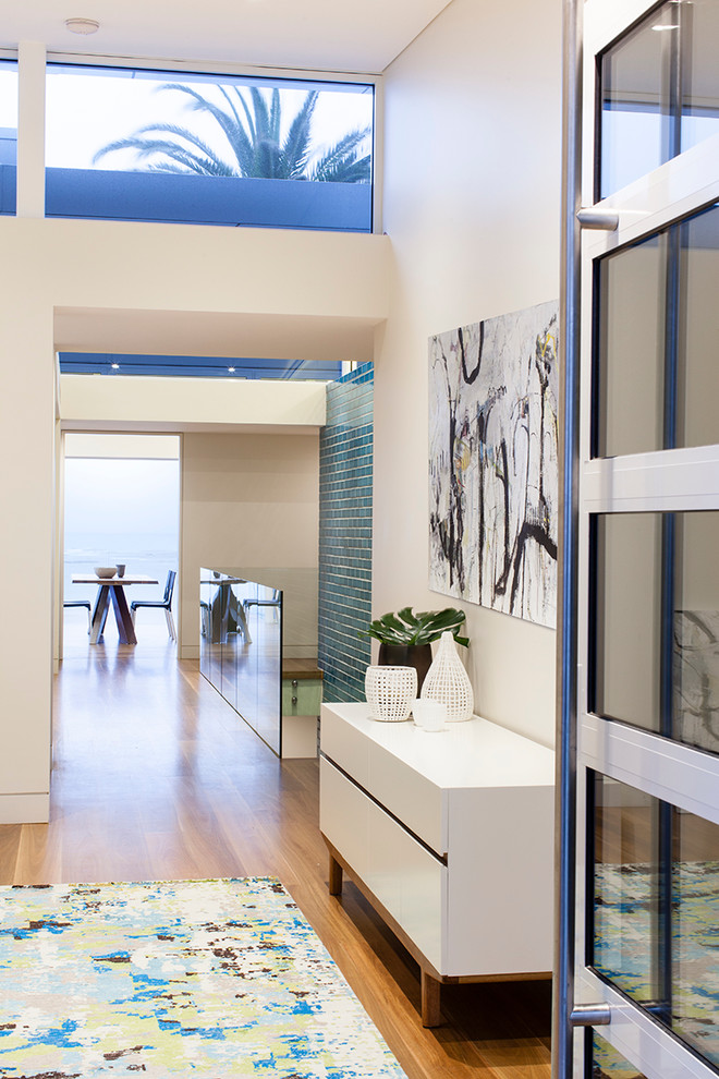 This is an example of a contemporary entry hall in Sydney with white walls, light hardwood floors, a single front door and a glass front door.