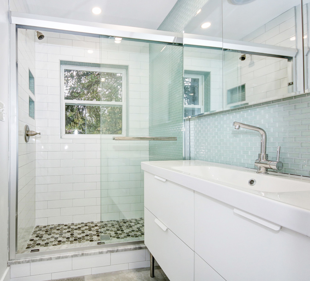 Photo of a mid-sized contemporary master bathroom in DC Metro with flat-panel cabinets, white cabinets, a corner shower, a one-piece toilet, blue tile, glass tile, white walls, ceramic floors, an integrated sink, solid surface benchtops, grey floor, a sliding shower screen and white benchtops.