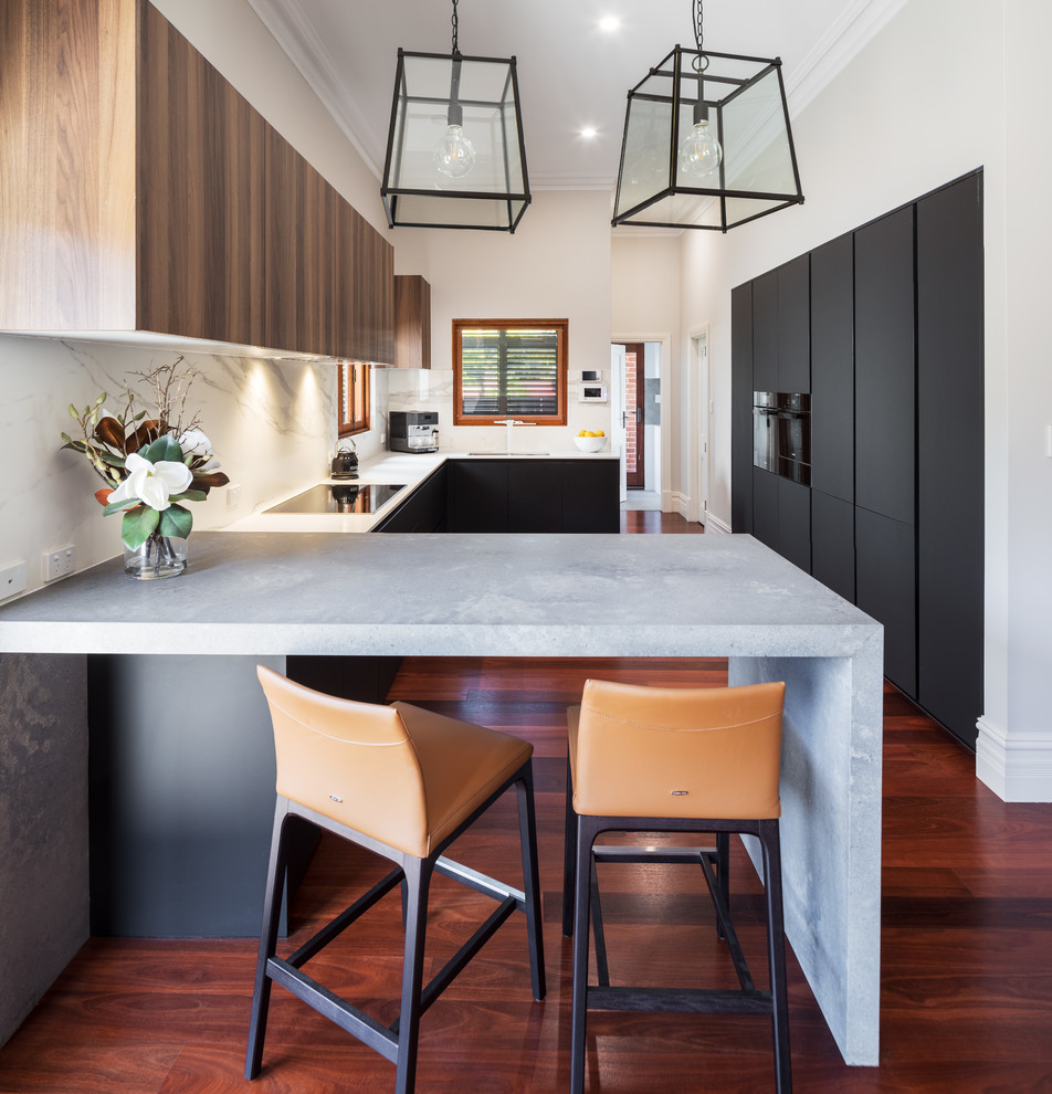 Inspiration for a large contemporary u-shaped kitchen in Perth with an undermount sink, flat-panel cabinets, black cabinets, white splashback, black appliances, dark hardwood floors, red floor and white benchtop.