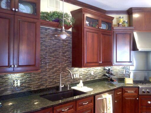 Example of a large transitional medium tone wood floor kitchen design with an undermount sink, raised-panel cabinets, dark wood cabinets, granite countertops, multicolored backsplash, matchstick tile backsplash, stainless steel appliances and an island