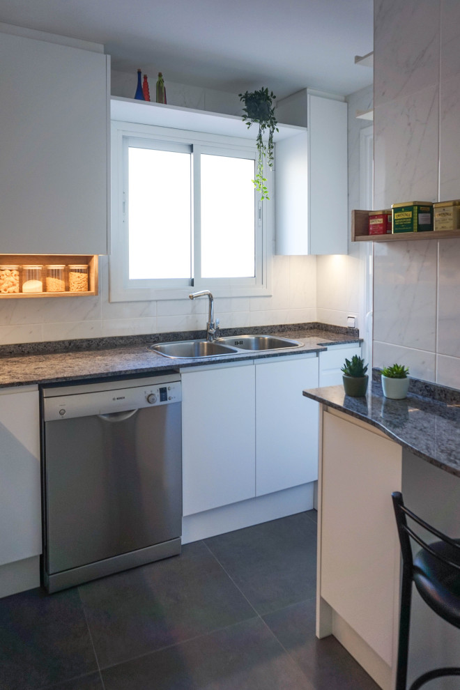 This is an example of a mid-sized contemporary l-shaped separate kitchen in Barcelona with a double-bowl sink, flat-panel cabinets, white cabinets, marble benchtops, white splashback, ceramic splashback, stainless steel appliances, porcelain floors, a peninsula, black floor and black benchtop.