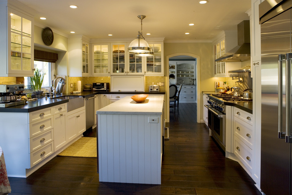 This is an example of a large traditional u-shaped eat-in kitchen in Los Angeles with a farmhouse sink, shaker cabinets, white cabinets, marble benchtops, green splashback, subway tile splashback, stainless steel appliances, dark hardwood floors, with island and brown floor.