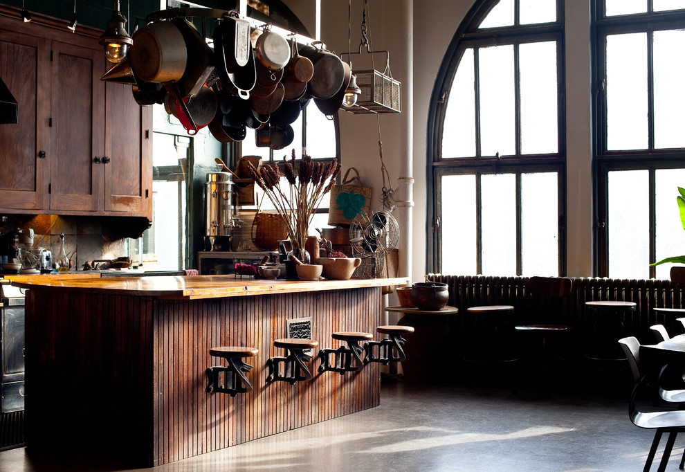 Cette photo montre une cuisine industrielle en L et bois foncé fermée et de taille moyenne avec un placard à porte shaker, un plan de travail en bois, un électroménager en acier inoxydable, sol en béton ciré et îlot.