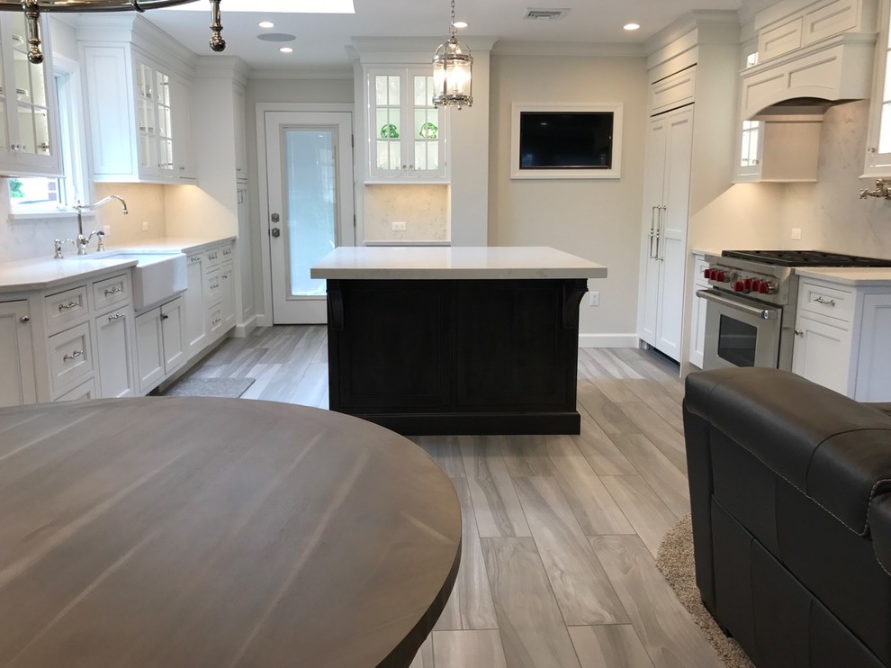 Open concept kitchen - mid-sized transitional u-shaped light wood floor and brown floor open concept kitchen idea with a farmhouse sink, recessed-panel cabinets, white cabinets, marble countertops, white backsplash, marble backsplash, stainless steel appliances and an island