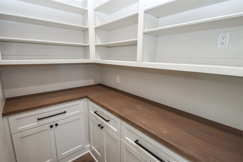 This is an example of a mid-sized transitional kitchen pantry in New Orleans with shaker cabinets, white cabinets, wood benchtops and brown benchtop.