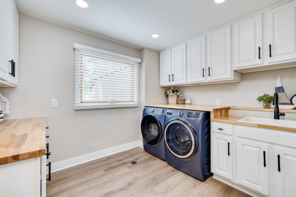Inspiration for a mid-sized galley dedicated laundry room in Other with an utility sink, raised-panel cabinets, white cabinets, wood benchtops, beige walls, vinyl floors, a side-by-side washer and dryer, brown floor and brown benchtop.