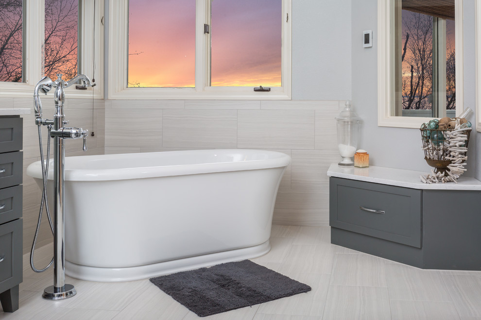 Example of a mid-sized transitional master white tile and porcelain tile porcelain tile freestanding bathtub design with an undermount sink, shaker cabinets, gray cabinets, quartz countertops, a one-piece toilet and gray walls