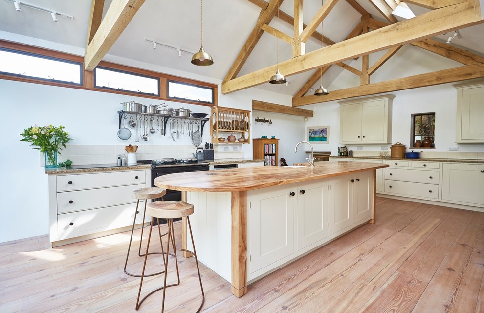 Inspiration for a mid-sized traditional galley open plan kitchen in Devon with a farmhouse sink, shaker cabinets, beige cabinets, wood benchtops, beige splashback, ceramic splashback, stainless steel appliances, medium hardwood floors, with island, brown floor and brown benchtop.