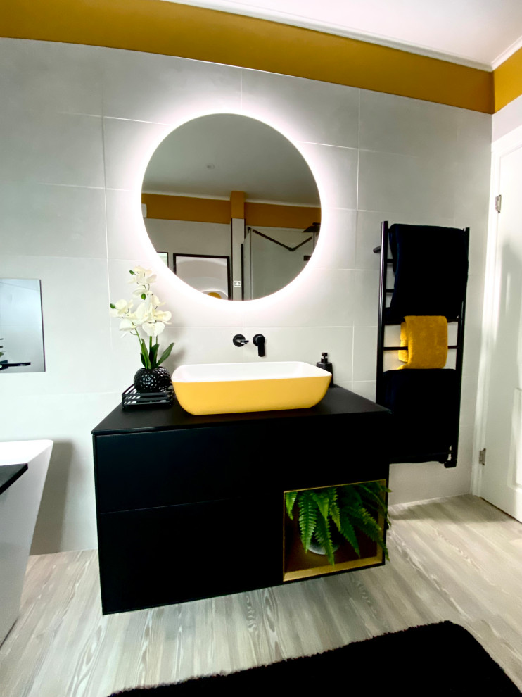 Источник вдохновения для домашнего уюта: большая детская ванная комната в современном стиле с плоскими фасадами, черными фасадами, инсталляцией, белой плиткой, керамогранитной плиткой, желтыми стенами, полом из ламината, настольной раковиной, стеклянной столешницей, коричневым полом, черной столешницей, отдельно стоящей ванной, открытым душем, душем с распашными дверями, тумбой под одну раковину и подвесной тумбой
