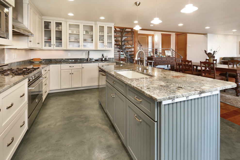 Inspiration for a beach style u-shaped kitchen in Seattle with an undermount sink, glass-front cabinets, white cabinets, granite benchtops, grey splashback, stone slab splashback, stainless steel appliances, concrete floors, a peninsula, green floor and grey benchtop.
