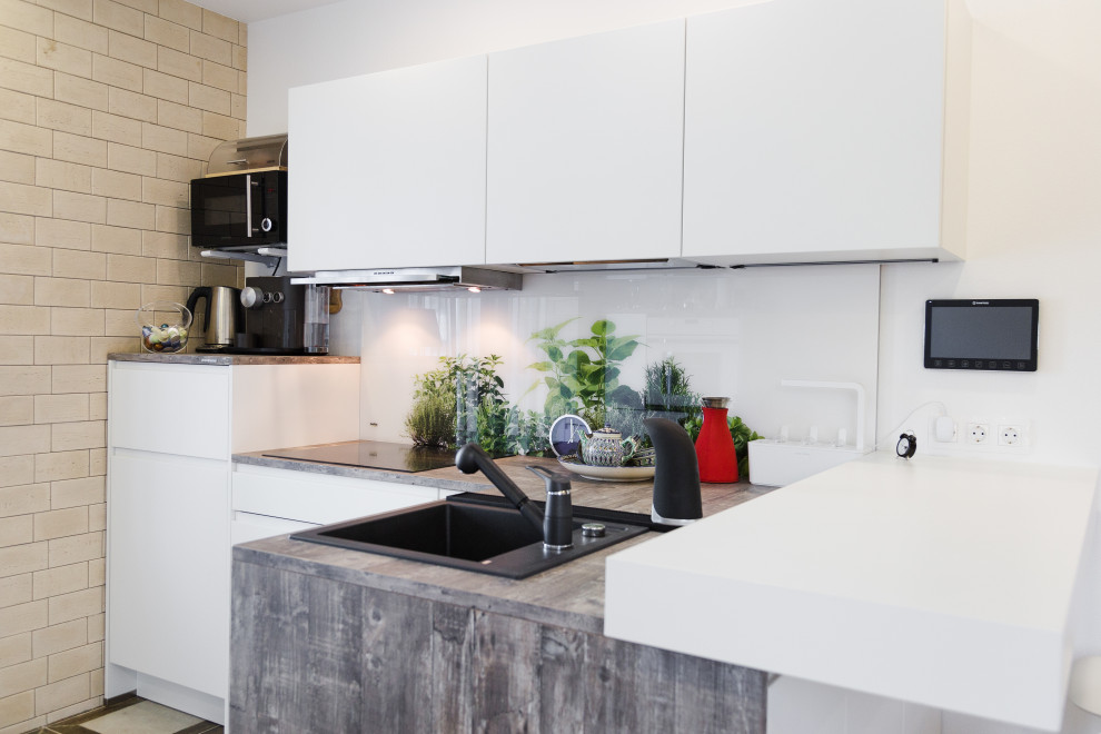 Inspiration for a small contemporary l-shaped kitchen in Other with a submerged sink, white cabinets, laminate countertops, white splashback, glass sheet splashback, black appliances and grey worktops.