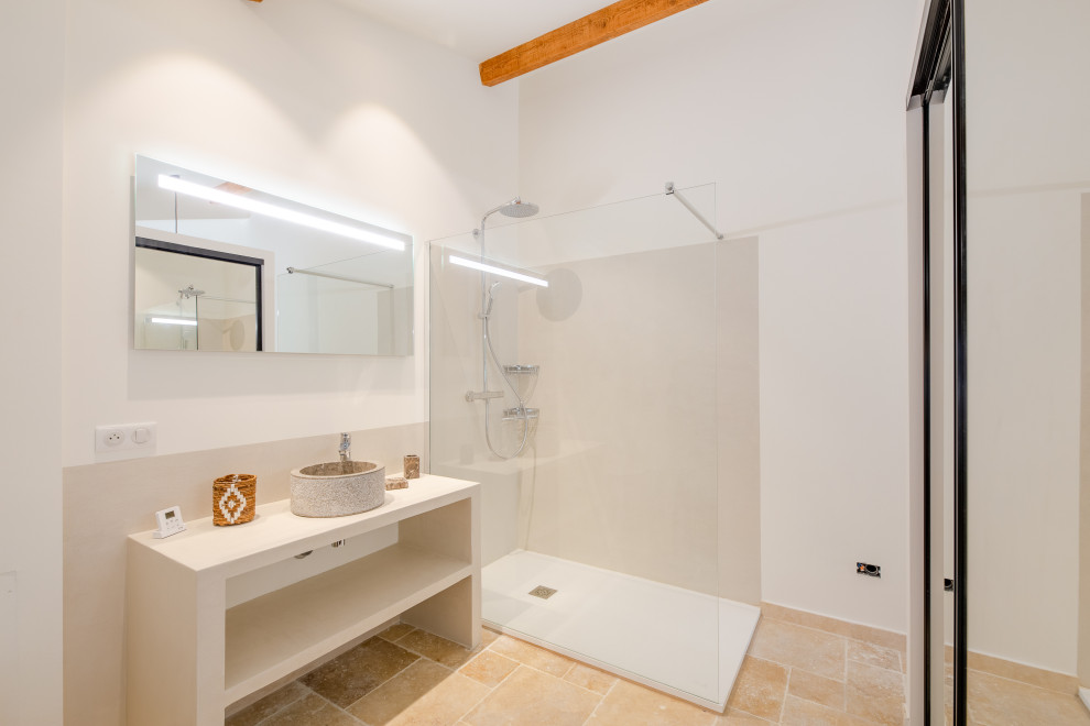 Cette photo montre une salle de bain bord de mer avec une douche ouverte, WC suspendus, un mur blanc, un sol en travertin, un plan vasque et un plan de toilette en béton.