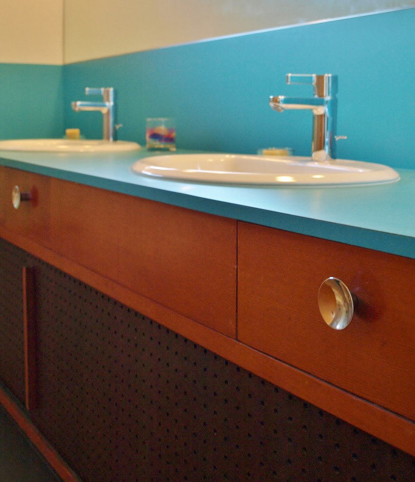 Photo of a mid-sized midcentury kids bathroom in Seattle with recessed-panel cabinets, medium wood cabinets, an alcove tub, a shower/bathtub combo, a two-piece toilet, gray tile, glass tile, white walls, ceramic floors, a drop-in sink and laminate benchtops.