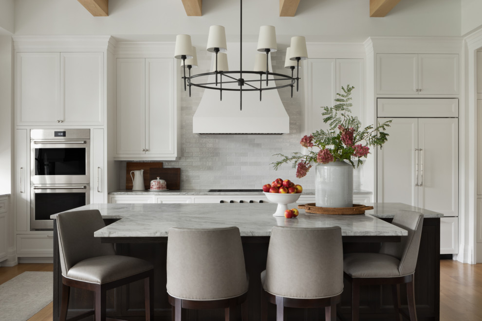 Design ideas for a country u-shaped kitchen in Milwaukee with recessed-panel cabinets, white cabinets, quartzite benchtops, white splashback, stone tile splashback, panelled appliances, light hardwood floors, with island, brown floor, grey benchtop and exposed beam.
