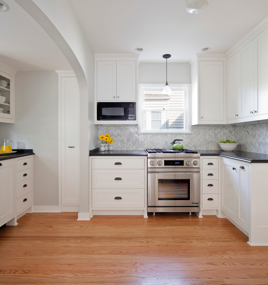 Design ideas for a large traditional u-shaped eat-in kitchen in Seattle with white cabinets, grey splashback, stainless steel appliances, a farmhouse sink, recessed-panel cabinets, granite benchtops, glass tile splashback, light hardwood floors and no island.