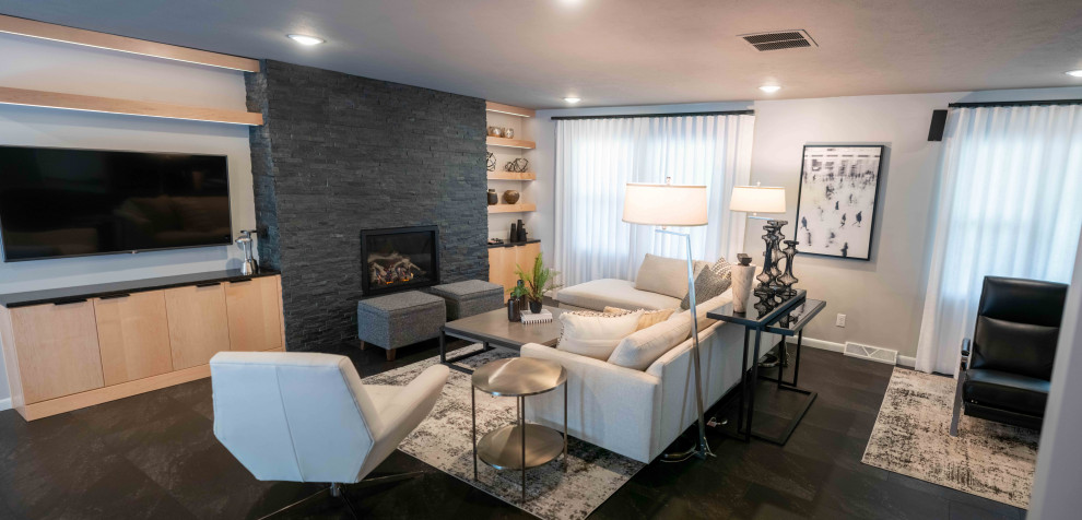 Пример оригинального дизайна: большая открытая гостиная комната в стиле ретро с серыми стенами, полом из винила, стандартным камином, фасадом камина из камня и черным полом
