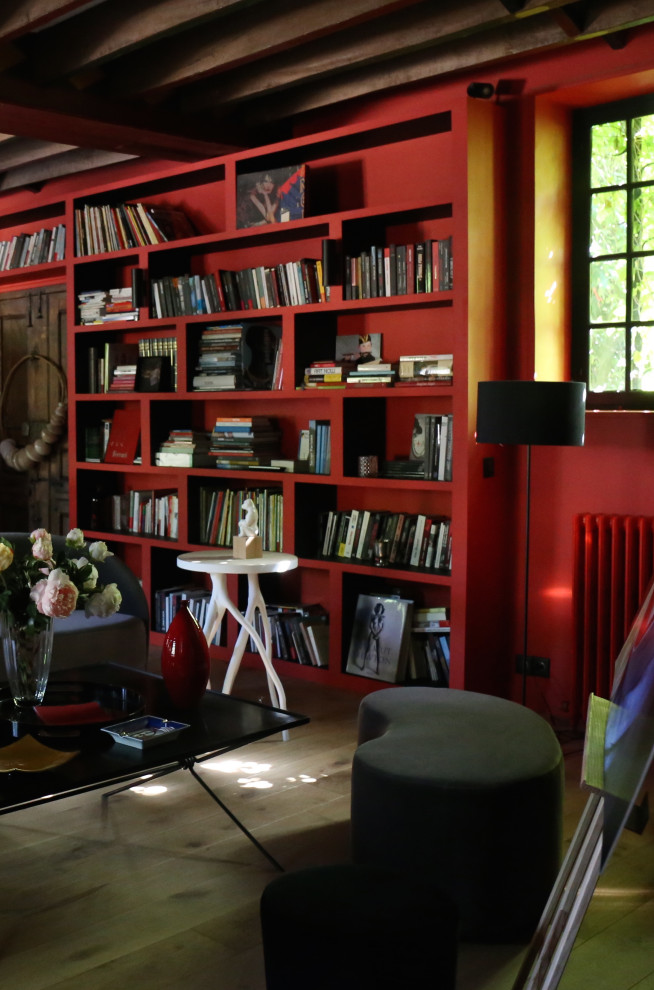 This is an example of a large country living room in Paris with a library, red walls, light hardwood floors and no tv.