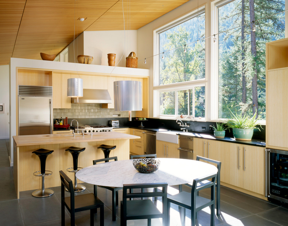 Inspiration for a contemporary l-shaped kitchen in Seattle with stainless steel appliances, a farmhouse sink, flat-panel cabinets, light wood cabinets, granite benchtops, black splashback and with island.