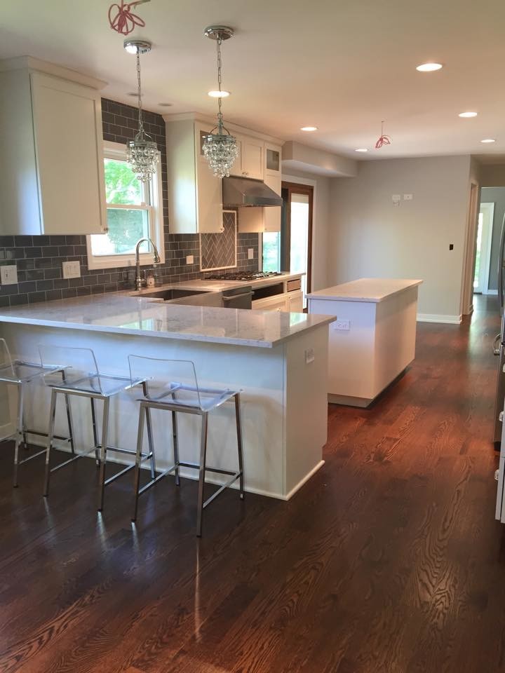Example of a large transitional u-shaped medium tone wood floor and brown floor open concept kitchen design in Chicago with a farmhouse sink, shaker cabinets, white cabinets, quartzite countertops, gray backsplash, subway tile backsplash, stainless steel appliances and an island