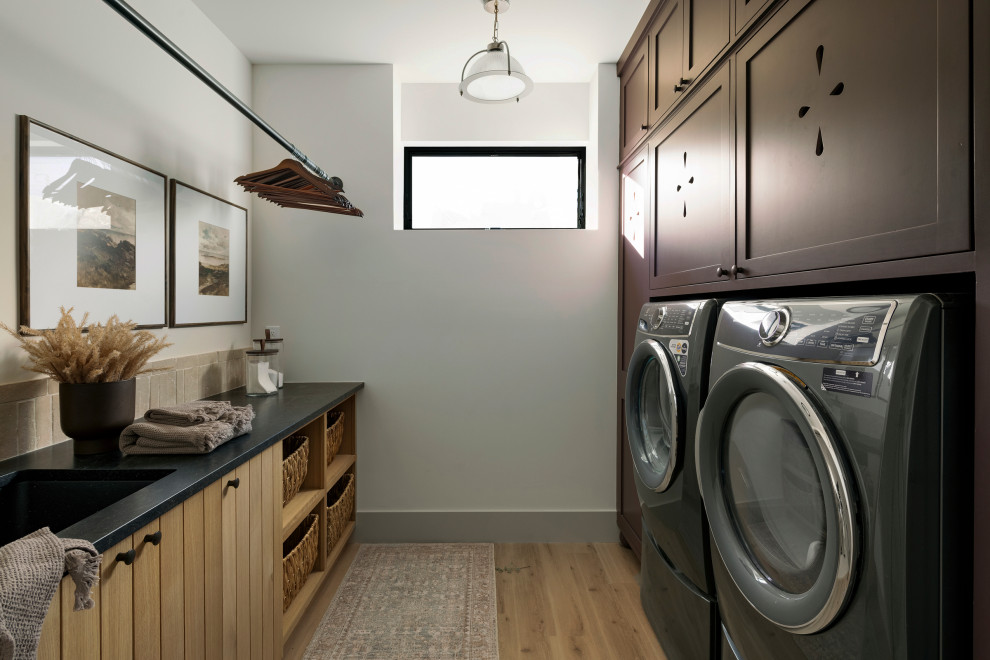 Country galley dedicated laundry room in Minneapolis with an undermount sink, shaker cabinets, brown cabinets, white walls, medium hardwood floors, a side-by-side washer and dryer, brown floor, black benchtop and granite benchtops.