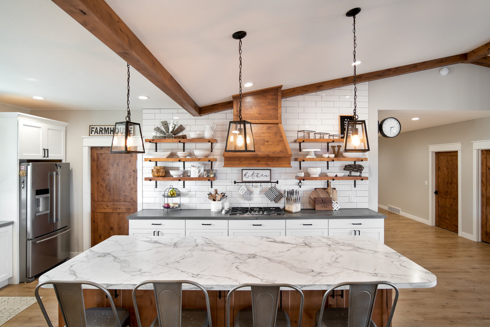 Photo of a large country eat-in kitchen in Other with a farmhouse sink, shaker cabinets, white cabinets, laminate benchtops, multi-coloured splashback, subway tile splashback, stainless steel appliances, medium hardwood floors, with island, brown floor and white benchtop.