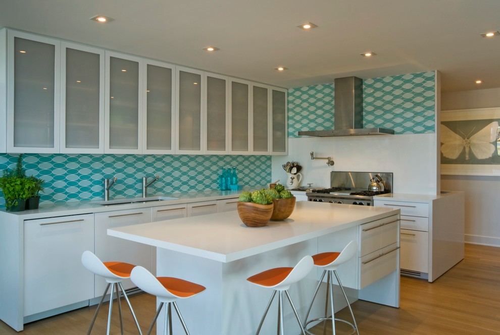 Photo of a beach style kitchen in New York with glass-front cabinets, white cabinets, blue splashback and stainless steel appliances.