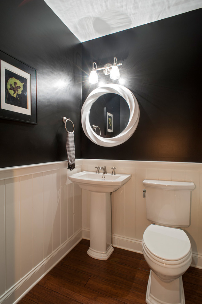 This is an example of a small transitional powder room in Other with a two-piece toilet, black walls, medium hardwood floors and a pedestal sink.