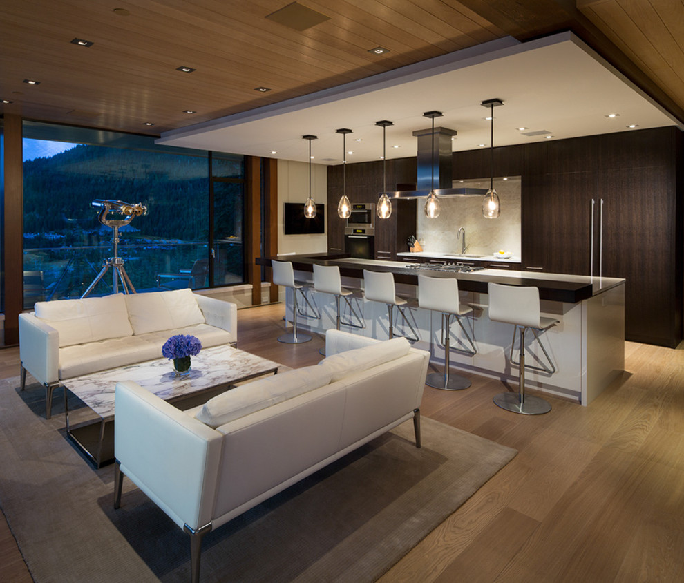 This is an example of a large modern single-wall open plan kitchen in Vancouver with an undermount sink, flat-panel cabinets, dark wood cabinets, solid surface benchtops, white splashback, stone slab splashback, stainless steel appliances, light hardwood floors and with island.