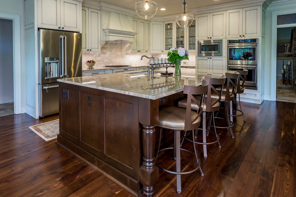 Inspiration for a large traditional l-shaped open plan kitchen in Charlotte with an undermount sink, flat-panel cabinets, beige cabinets, granite benchtops, beige splashback, travertine splashback, stainless steel appliances, medium hardwood floors, with island and brown floor.