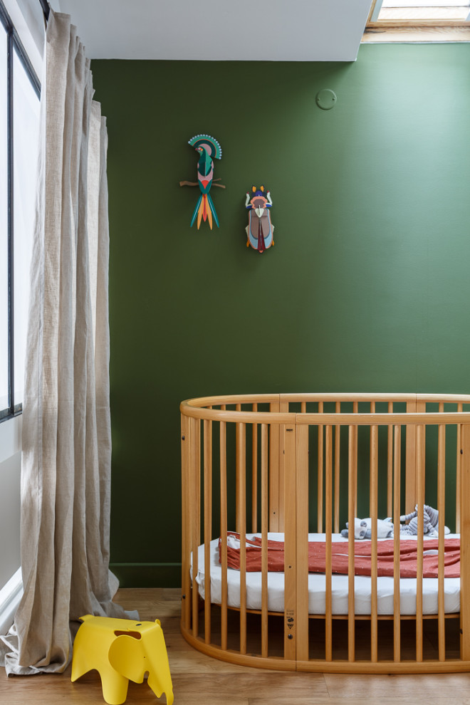 Ejemplo de habitación de bebé neutra urbana de tamaño medio con paredes verdes, suelo de madera en tonos medios y suelo marrón