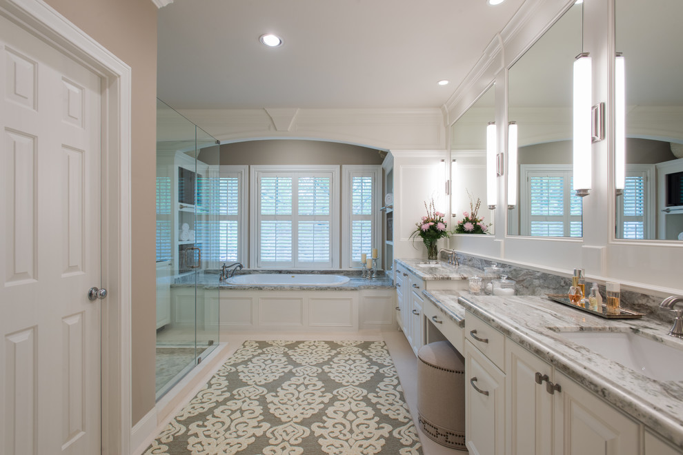 Photo of a large transitional master bathroom in Houston with raised-panel cabinets, white cabinets, a drop-in tub, a one-piece toilet, beige tile, porcelain tile, white walls, limestone floors, an undermount sink and engineered quartz benchtops.