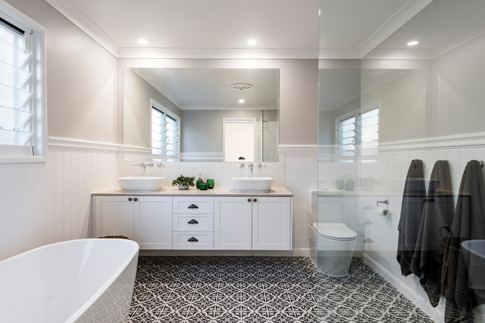 Inspiration for a mid-sized beach style master bathroom in Gold Coast - Tweed with a freestanding tub, grey walls, shaker cabinets, white cabinets, an open shower, a one-piece toilet, white tile, ceramic tile, ceramic floors, a drop-in sink, engineered quartz benchtops, black floor and an open shower.