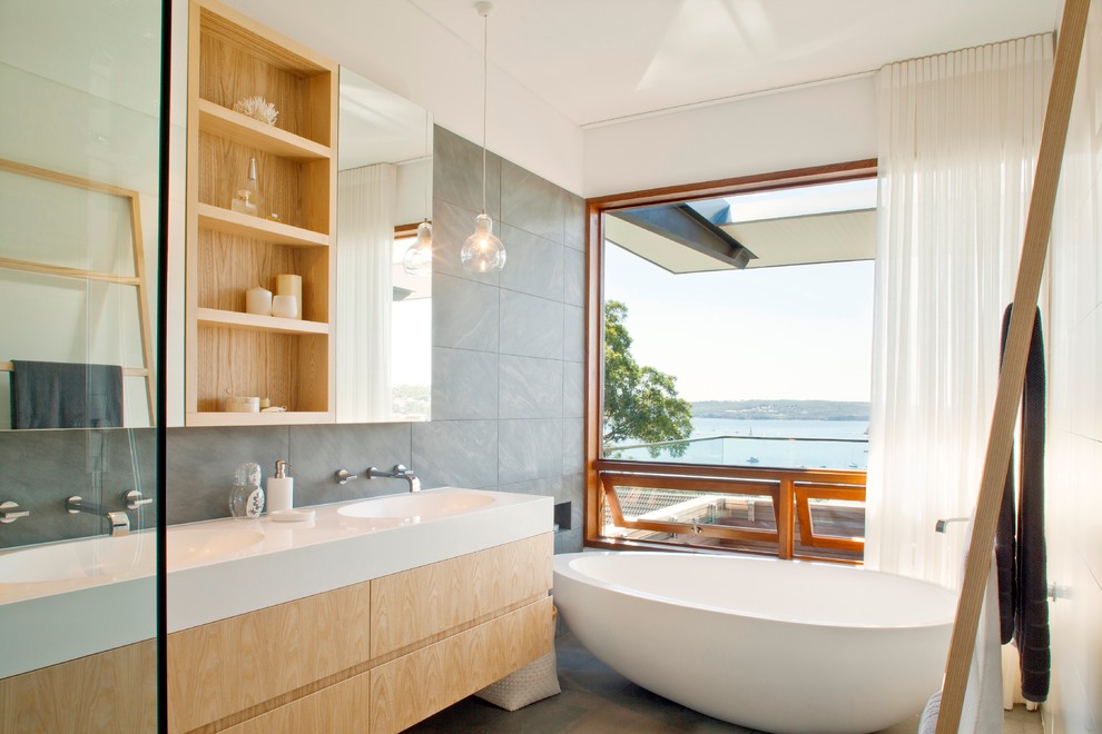 Design ideas for a contemporary bathroom in Sydney with an integrated sink, flat-panel cabinets, light wood cabinets, a freestanding tub, gray tile, grey walls and ceramic floors.