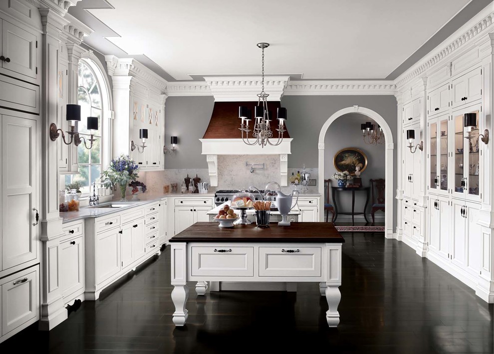 This is an example of a large traditional l-shaped kitchen pantry in New York with white cabinets, white splashback, dark hardwood floors, recessed-panel cabinets, marble benchtops, stone slab splashback, stainless steel appliances and multiple islands.