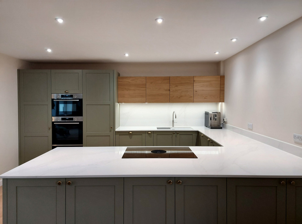 Inspiration for a medium sized classic u-shaped open plan kitchen in Other with a double-bowl sink, shaker cabinets, green cabinets, quartz worktops, white splashback, engineered quartz splashback, stainless steel appliances, plywood flooring, a breakfast bar, beige floors and white worktops.