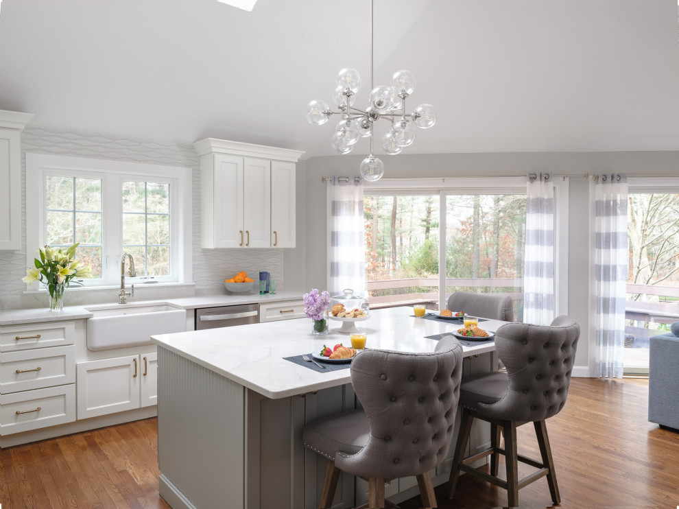 Example of a large transitional l-shaped medium tone wood floor and brown floor kitchen design in Boston with white cabinets, white backsplash, an island and white countertops