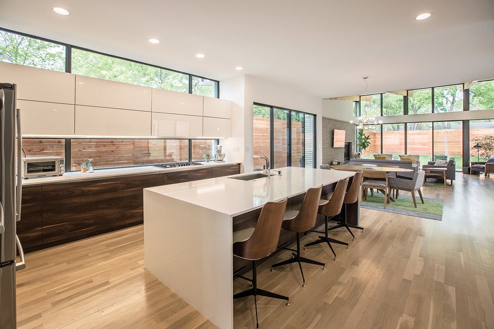 Design ideas for a midcentury open plan kitchen in Dallas with an undermount sink, flat-panel cabinets, white cabinets, window splashback, light hardwood floors, with island, stainless steel appliances and brown floor.