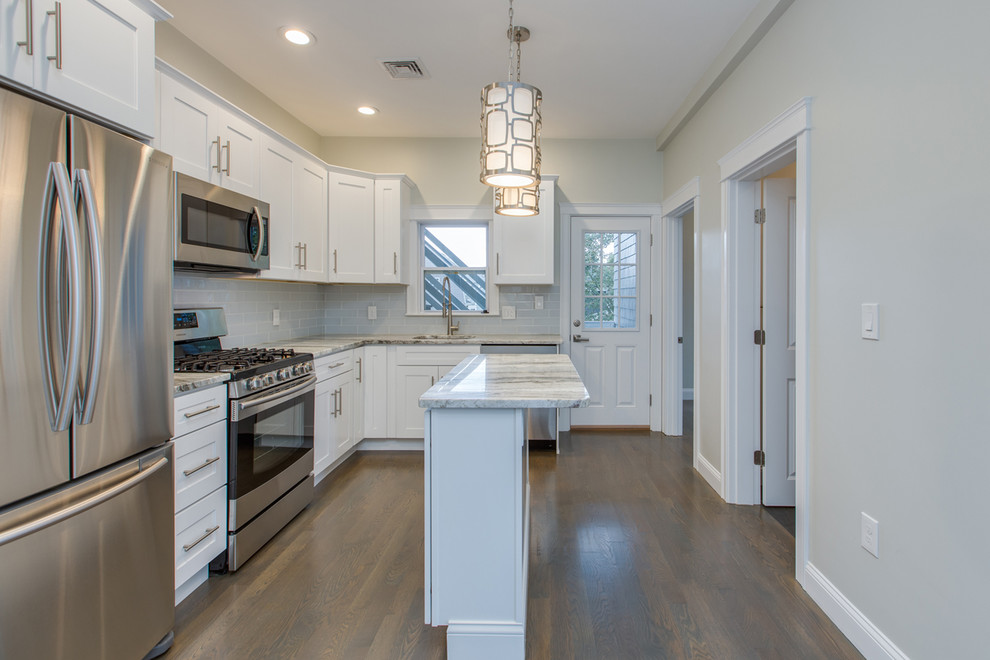 Example of a mid-sized transitional l-shaped dark wood floor and brown floor enclosed kitchen design in Boston with an undermount sink, shaker cabinets, white cabinets, marble countertops, gray backsplash, subway tile backsplash, stainless steel appliances, an island and white countertops