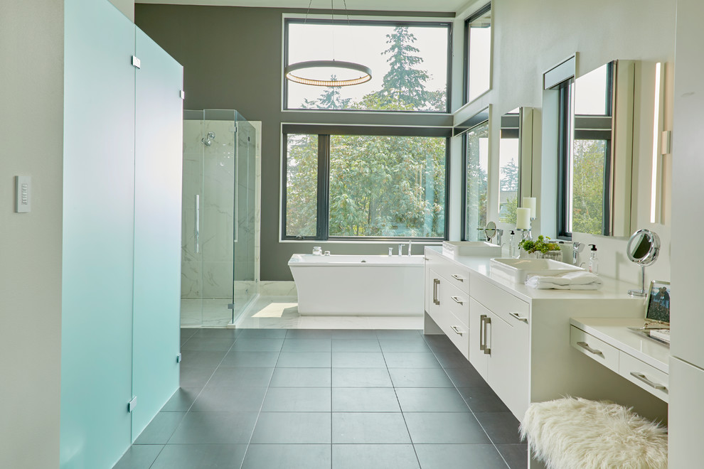 This is an example of an expansive contemporary master bathroom in Seattle with flat-panel cabinets, white cabinets, a freestanding tub, engineered quartz benchtops, grey floor, a hinged shower door, white benchtops, white tile, grey walls and a vessel sink.