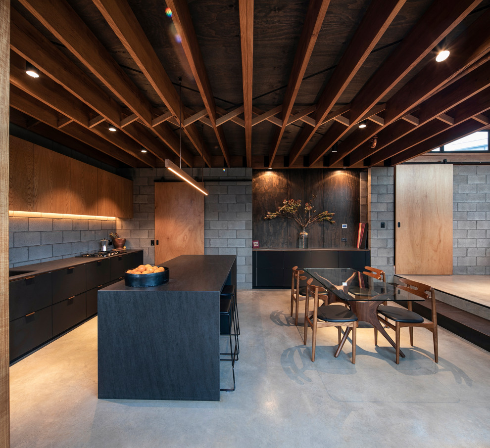 Photo of a contemporary galley open plan kitchen in Sydney with flat-panel cabinets, black cabinets, grey splashback, concrete floors, with island, grey floor and black benchtop.