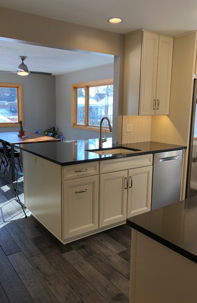 Inspiration for a transitional eat-in kitchen in Minneapolis with an undermount sink, recessed-panel cabinets, beige cabinets, quartz benchtops, white splashback, ceramic splashback, stainless steel appliances, porcelain floors, a peninsula, grey floor and black benchtop.