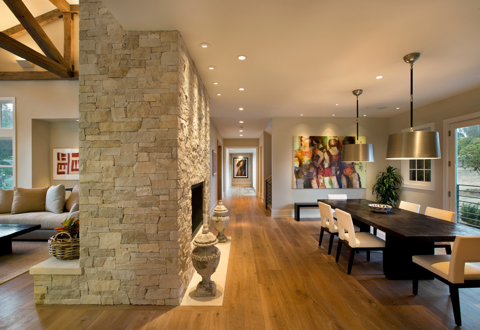 This is an example of a country dining room in San Francisco with beige walls, medium hardwood floors, a standard fireplace and a stone fireplace surround.
