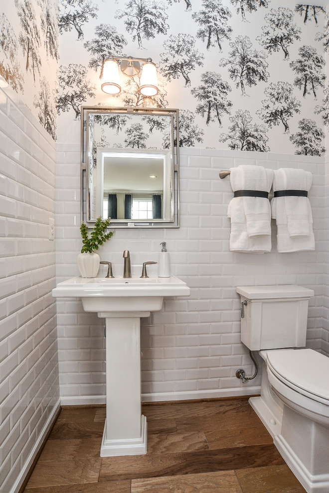 Photo of a traditional powder room in DC Metro with a two-piece toilet, white tile, subway tile, medium hardwood floors, a pedestal sink and brown floor.