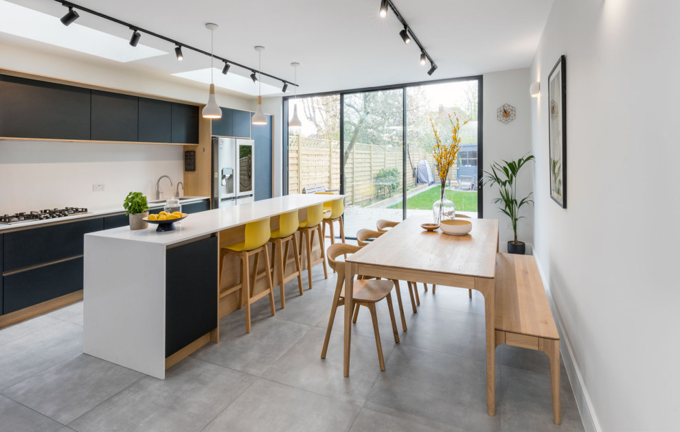 Contemporary galley eat-in kitchen in London with an undermount sink, flat-panel cabinets, black cabinets, quartz benchtops, white splashback, stainless steel appliances, concrete floors, with island, grey floor and white benchtop.
